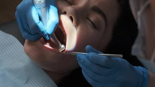 Dentist performs dental procedure on caucasian female patient with dental turbine handpiece, mirror and saliva ejector