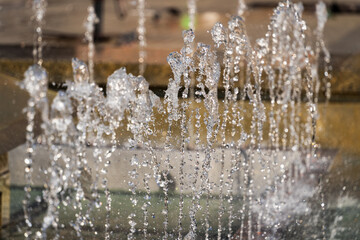 Selective focus, water jets of the city fountain on a sunny day on a blurred background, hot summer...