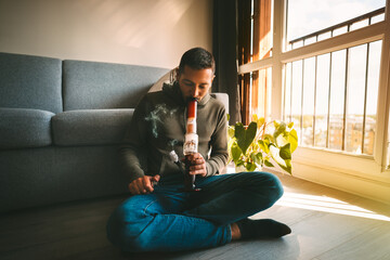 Man smoking bong and inhaling the smoke at home. Man smoking pot, medical marijuana or cannabis...