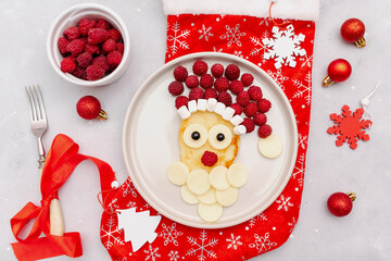 Christmas Santa Claus face shaped pancake with sweet fresh raspberry berry and cheese on plate on gray background for kids baby children breakfast dinner. xmas food with new year decorations close up.
