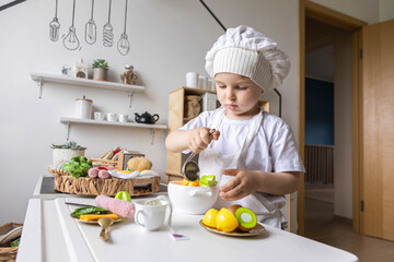 Cute baby boy chef uniform cooking playthings vegetable salad at childish kitchen enjoy childhood