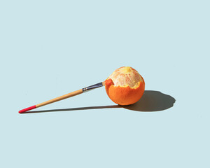 Orange and painting brush on pastel light blue background. Minimalistic fruit concept. Creative summer nature composition.