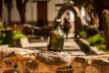 Horizontal format photograph of a bottle of green wine without content on a small white wall in a square in the town of Cachi, Salta, Argentina.