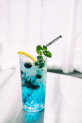 Colorful summery blue curacao cocktail on a white table with trendy shadows. Refreshing drinks with...