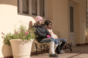 teenage girls sitting on wooden bench in sunny autumn afternoon
