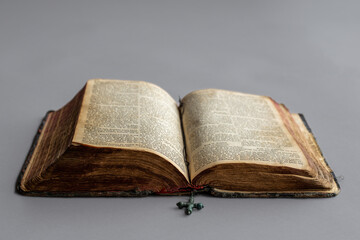 An old open bible with an old cross is lying on the table