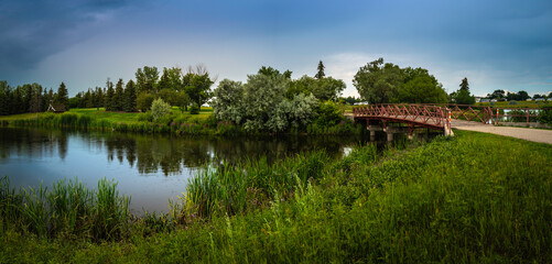Wascana Creek pond and bridge adjacent to the tranquil hilly meadow with footpaths at A.E. Wilson Park in Regina, Saskatchewan, Canada. A rainy day landscape at the city park.