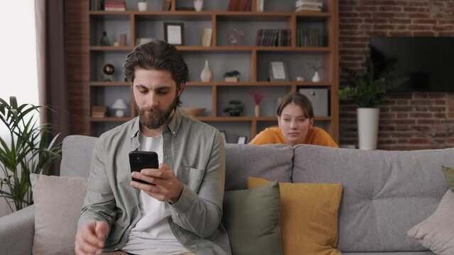 Jealous young woman trying to have a peek into the boyfriend smartphone. Cheater man dating online, girlfriend is spying, trying to read messages on the mobile phone while he is not watching.