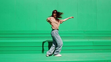 Young woman dancing hip hop on green background wall. Modern dance choreography. Female professional dancer showing dance movings. Musical video. - Powered by Adobe
