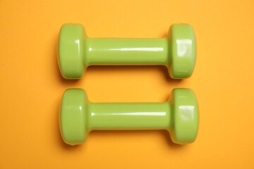 Dumbbells on orange background, flat lay. Sport equipment