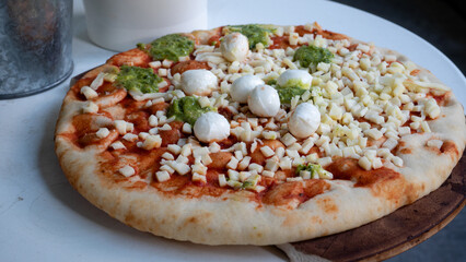 Store bought, uncooked mozzarella and pesto flavored pizza. This oven ready family sized pizza is also covered in cheese, basil and tomato sauce. Italian pizza and fast food concept.