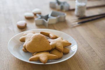 A white plate of traditional ginger biscuits stands on a wooden table. Brushes for drawing on gingerbread, forms for gingerbread in the form of hearts and stars.