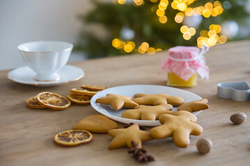 Plate with traditional ginger cookies in front of a Christmas tree with a herald of lights. 