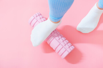 Female leg rolls a massage foam roller close-up on a pink background.