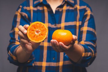 Close-up of hands holding oranges while standing on a gray background