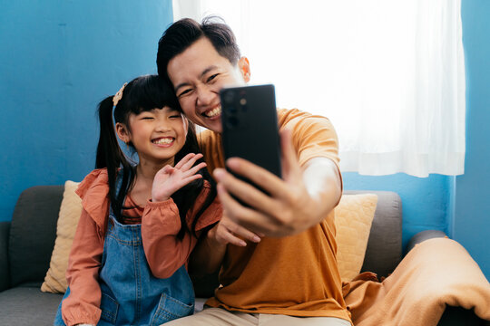 Asian Family Of Father And Daughter Taking A Selfie Photo With Mobile Phone At Home