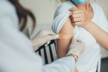 Doctor in rubber protective gloves putting adhesive bandage on patient's arm after vaccination. Pandemic prevention. Coronavirus vaccination. Coronavirus