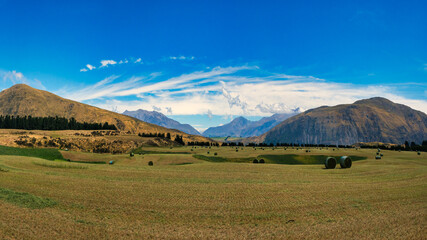 Fototapeta na wymiar Hay bales sitting on agricultural farm grazing fields beneath the Southern Alps