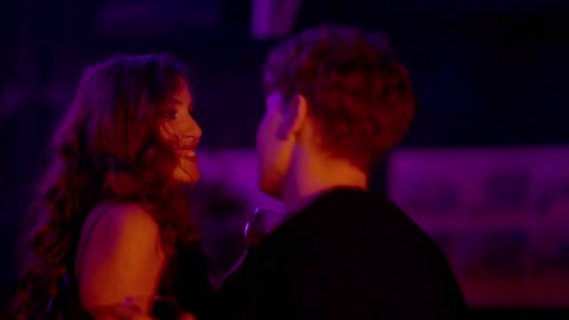 Close-up of a sensual couple flirting, kissing under neon lights in a nightclub. The couple drinks alcohol and kisses. Night club