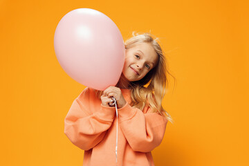 funny, happy girl stands peeking out from behind a pink balloon on an orange background in orange...