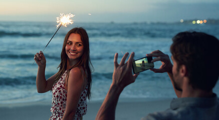 Beautiful woman holding sparkler posing for photo on romantic beach celebrating new years eve at...