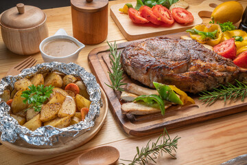 Barbecue Tomahawk Steak on wooden plate.Grilled tomahawk ribeye steak with baked potatoes ,mashroom, roasted sweet peppers and tomato ready to serve. 