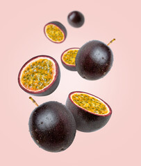Purple passion fruit with water droplets and half sliced flying in the air isolated on pink background.