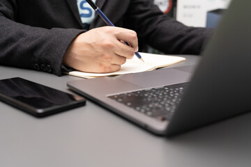 organizing work process in own notepad enjoying tasty cappuccino sitting indoors at laptop computer. working on desk with laptop and smartphone.