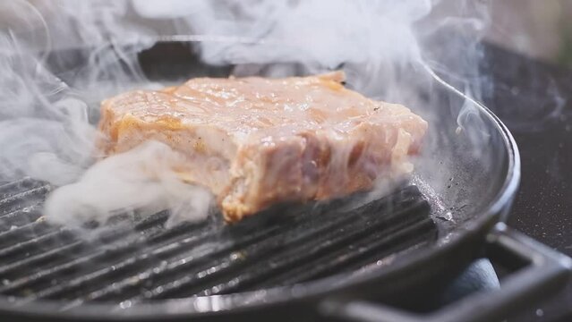 Chef puts pork chop on a grill pan.
