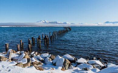 Obraz premium muelle antiguo de madera deteriorada con el pasar de los años y el agua de mar, con montañas nevadas y nubes bajas, costa nevada con rocas con nieve.