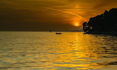 View from the bay in the city of Cavtat-Croatia, late sunset with a small boat in the background, June, colors: gray, black and gold