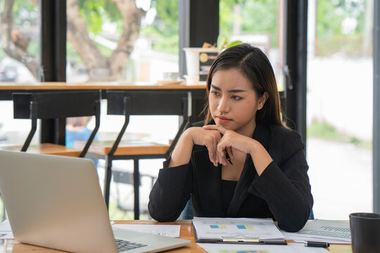 Thoughtful Asian businesswoman in tension and looking for problem solution sitting at workplace desk while working on a laptop in an office.