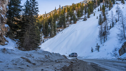 The road winds between snow-capped mountains. Coniferous forest grows on the slopes. The car is parked on the highway. Altai. Red Gate
