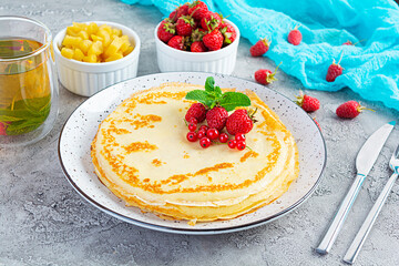 Pancakes with caramelized apples, raspberries, strawberries and red currants. Brunch with green tea and crepes.