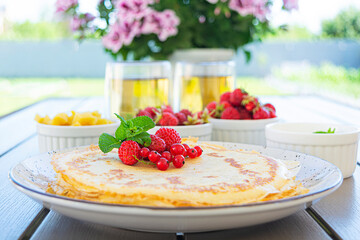 Pancakes with caramelized apples, raspberries, strawberries and red currants. Brunch with green tea and crepes.