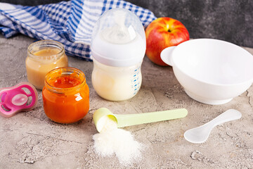 Bowl with vegetables puree and bottle of baby food on gray background