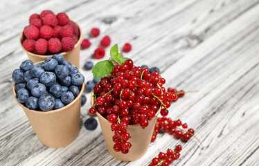 Summer composition. Juicy summer berries in craft paper cups. Blueberries, red currants, raspberries. Light wooden background.