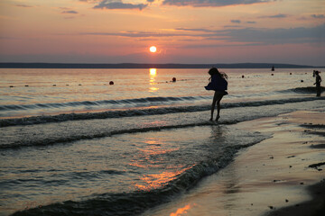 Naklejka premium A little girl jumps on the waves against the background of sunset