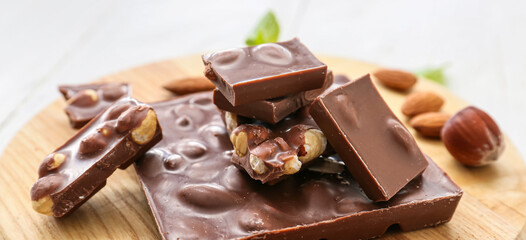 Pieces of tasty chocolate with hazelnuts on table, closeup
