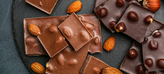 Pieces of tasty chocolate with hazelnuts and almonds on dark table, top view