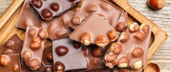 Pieces of tasty chocolate with hazelnuts on wooden table, top view