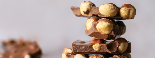 Pieces of tasty chocolate with hazelnuts on light background, closeup