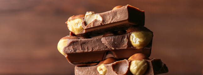 Pieces of tasty chocolate with hazelnuts on brown background, closeup