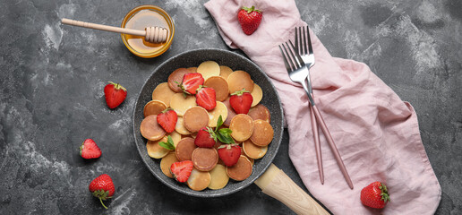 Composition with frying pan of mini pancakes, strawberry and honey on grunge background, top view