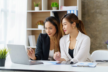 Two professional Asian business women discuss work using a laptop computer to work in the office.