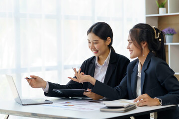 Two professional Asian business women discuss work using a laptop computer to work in the office.