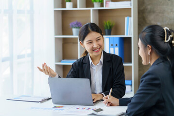 Two professional Asian business women discuss work using a laptop computer to work in the office.