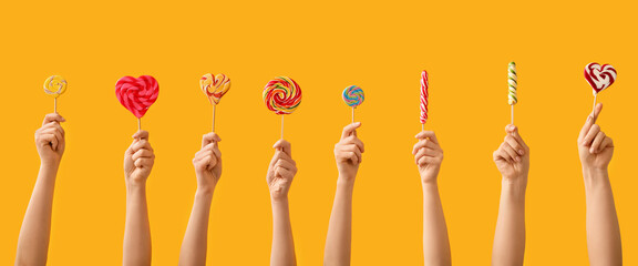 Fototapeta premium Many hands with sweet lollipops on yellow background