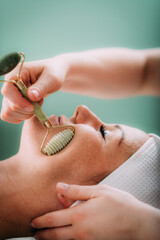 Guasha face massage in beauty salon, massage technique for stimulating pressure points on the face, using jade stone roller © Microgen