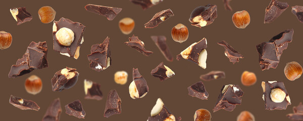 Falling pieces of chocolate with hazelnuts on brown background